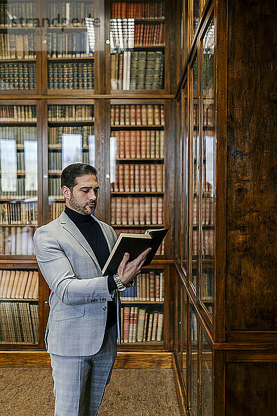 Geschäftsmann  der in einer Bibliothek steht und ein Buch liest