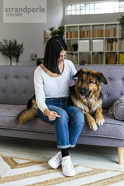 Frau mit deutschem Schäferhund sitzt zu Hause auf dem Sofa