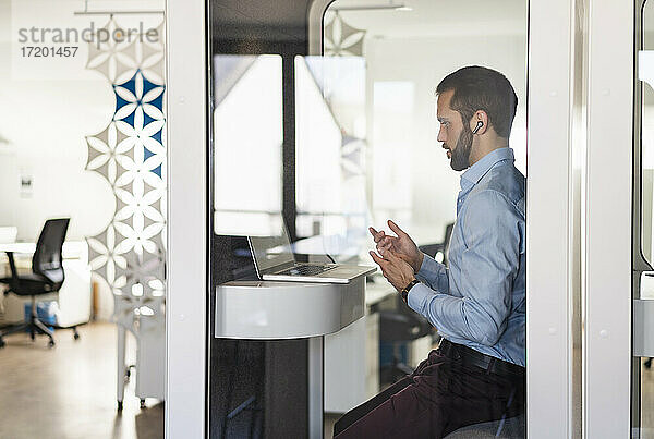 Geschäftsmann im Gespräch über Videoanruf über Laptop  während er in einer Telefonzelle im Büro sitzt