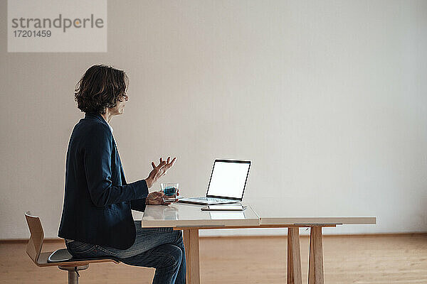 Frau gestikuliert bei der Verwendung eines Laptops auf dem Tisch im Büro zu Hause