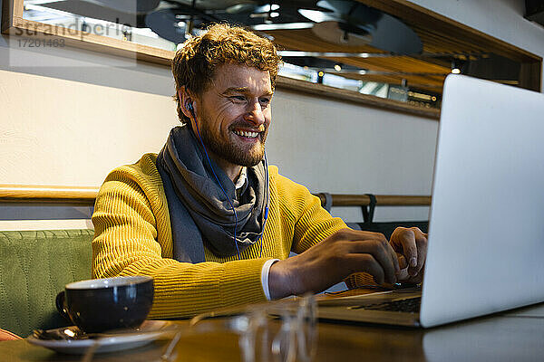 Glücklicher männlicher Unternehmer  der einen Laptop während eines Videogesprächs in einem Café benutzt