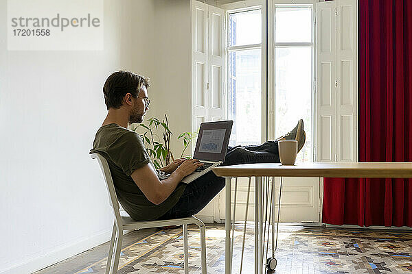 Junger männlicher Unternehmer arbeitet am Laptop  während er am Tisch im Büro sitzt