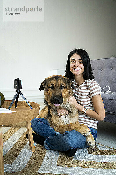 Lächelnde junge Frau mit Hund auf dem Schoß im Wohnzimmer