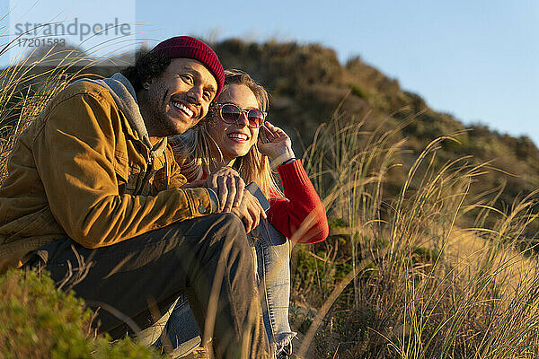 Lächelndes Paar  das auf einer Sanddüne sitzt und wegschaut