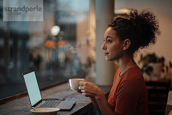 Frau mit Laptop  die in einem Café sitzt und Kaffee trinkt