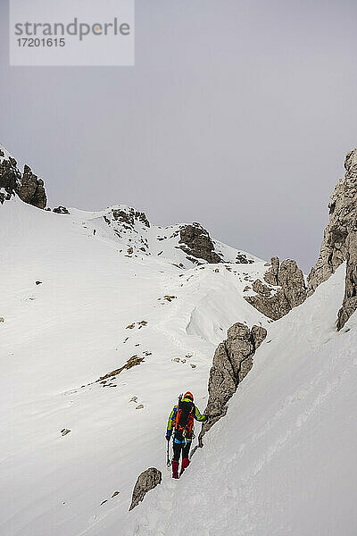 Älterer Wanderer an einem Felsen auf einem schneebedeckten Berg