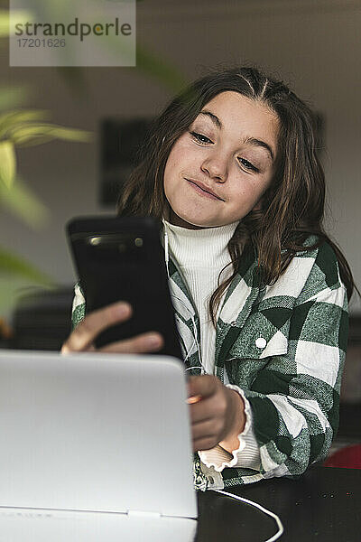 Lächelndes Mädchen  das ein Mobiltelefon am Tisch in einem Haus benutzt