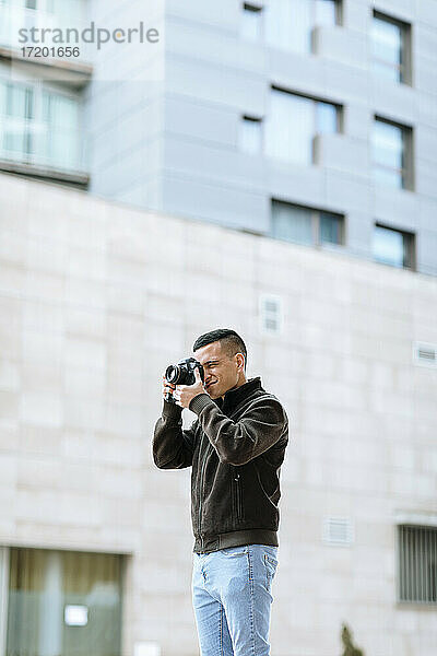 Junge männliche Fachkraft  die durch die Kamera fotografiert  während sie vor einem Gebäude steht