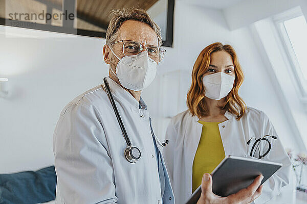 Männlicher Arzt mit digitalem Tablet  der neben einem Mitarbeiter in einer Klinik steht