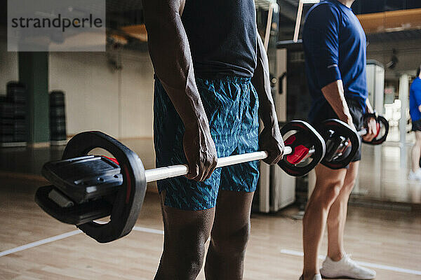 Männliche Athleten  die eine Langhantel halten  während sie im Fitnessstudio trainieren