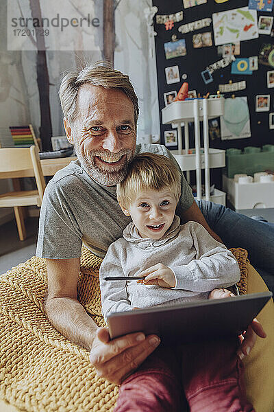 Lächelnder Vater und Sohn mit digitalem Tablet im Schlafzimmer