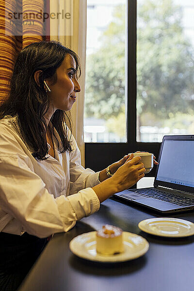 Junge Berufstätige hält eine Tasse Kaffee in der Hand  während sie in einem Café sitzt