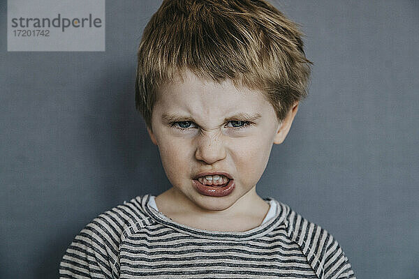 Wütender Junge mit Grimasse auf grauem Hintergrund