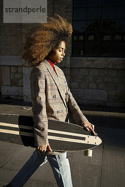 Junge Frau mit braunem Haar geht mit Skateboard