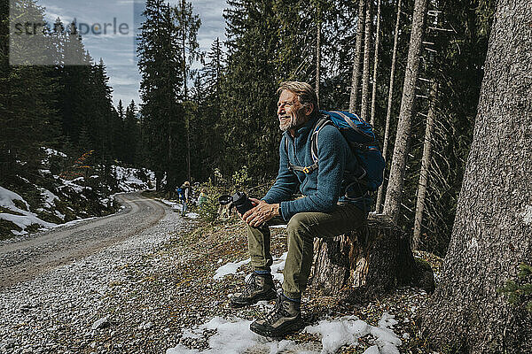 Lächelnder reifer Mann  der wegschaut  während er eine Wasserflasche gegen Bäume im Salzburger Land  Österreich  hält