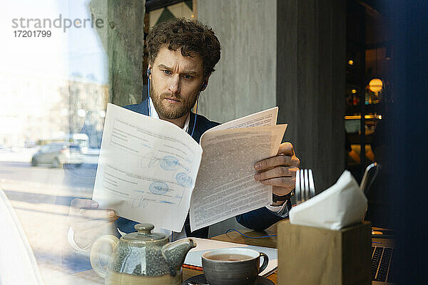 Männlicher Unternehmer prüft Strategie  während er im Café sitzt  gesehen durch Glas