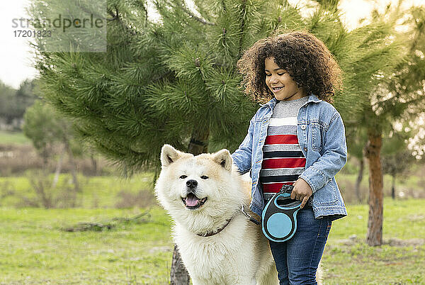 Lächelnder  lockig behaarter Junge genießt mit Hund in der Natur