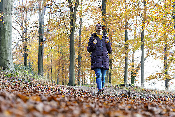 Lächelnde Frau  die einen Rucksack hält und im Herbstwald nach oben schaut