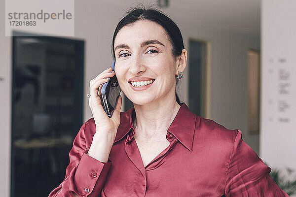 Lächelnde Geschäftsfrau  die zu Hause mit ihrem Smartphone telefoniert