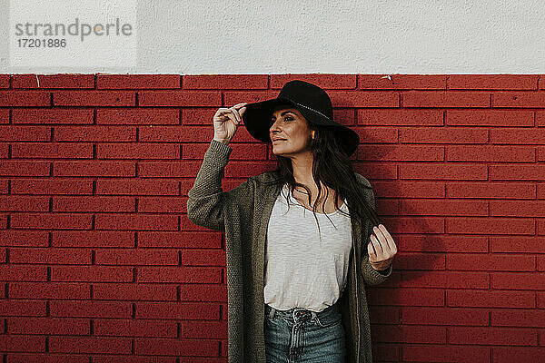 Frau mit Hut schaut weg  während sie an einer roten Backsteinmauer steht