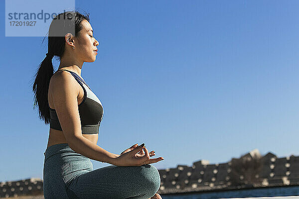 Junge Sportlerin meditiert bei der Übung des Lotussitzes an einem sonnigen Tag