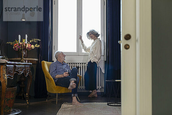 Älterer Mann mit Weinglas  der eine Frau betrachtet  die zu Hause am Fenster steht