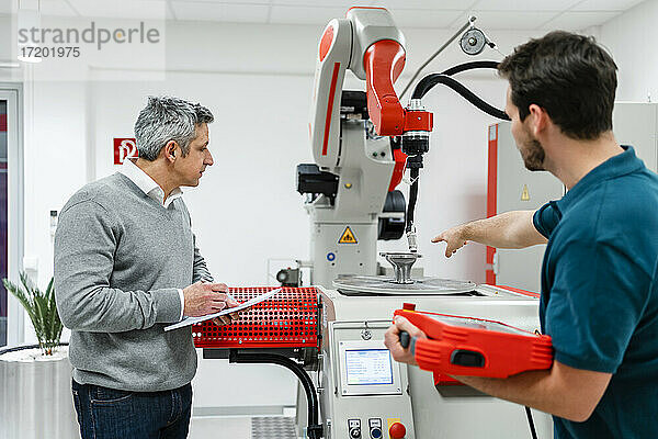 Ingenieur  der auf eine Maschine zeigt  während er sich mit einem Kollegen in der Industrie unterhält