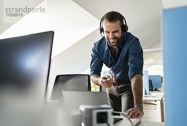 Lächelnde Fachkraft  die über Kopfhörer einen Videoanruf über einen Laptop im Büro führt