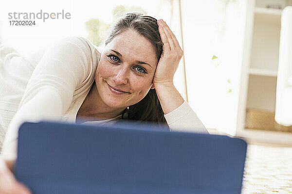 Lächelnde Frau mit digitalem Tablet im Wohnzimmer liegend