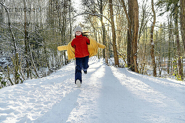 Glückliches Mädchen in warmer Kleidung  das im Winter im Schnee läuft