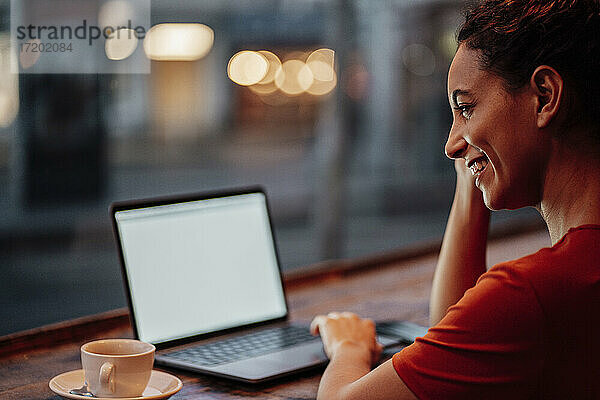 Lächelnde Frau  die einen Laptop benutzt  während sie in einem Café sitzt