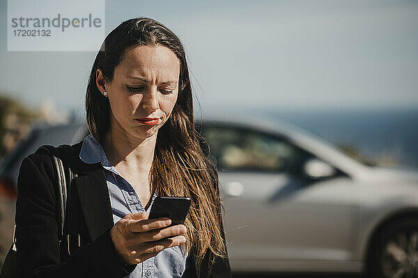 Mittlere erwachsene Geschäftsfrau  die an einem sonnigen Tag ihr Mobiltelefon überprüft