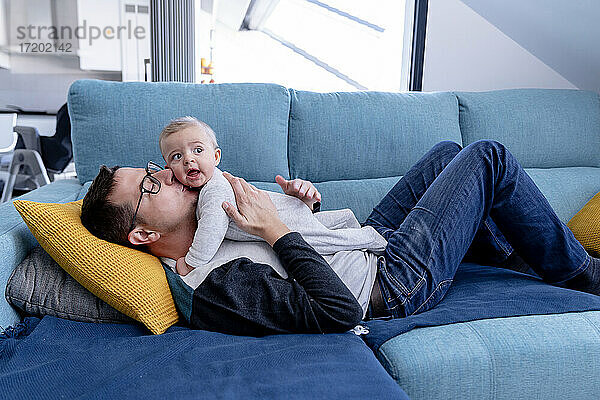 Zärtlicher Vater küsst seinen kleinen Sohn  während er auf dem Sofa im Wohnzimmer liegt