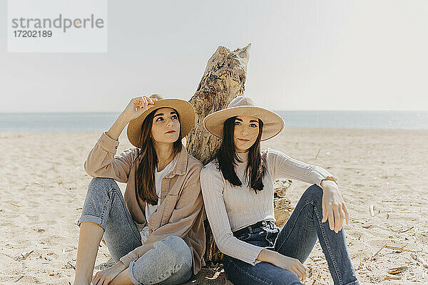 Weibliche Zwillinge sitzen Seite an Seite am Strand an einem sonnigen Tag