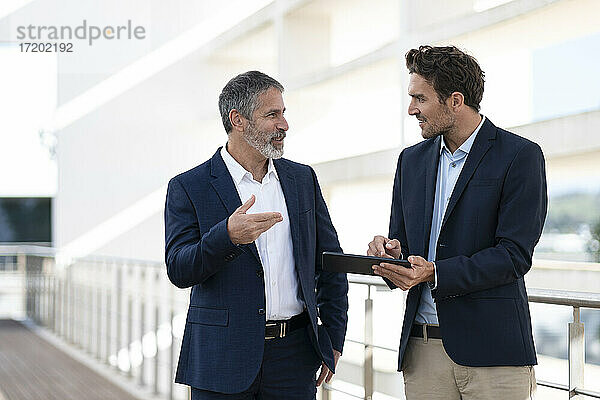 Geschäftsleute diskutieren über digitale Tablette  während sie auf der Terrasse eines Bürogebäudes stehen