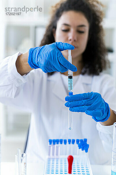 Junge Wissenschaftlerin beim Mischen einer Lösung im Reagenzglas mit einer Spritze im Labor