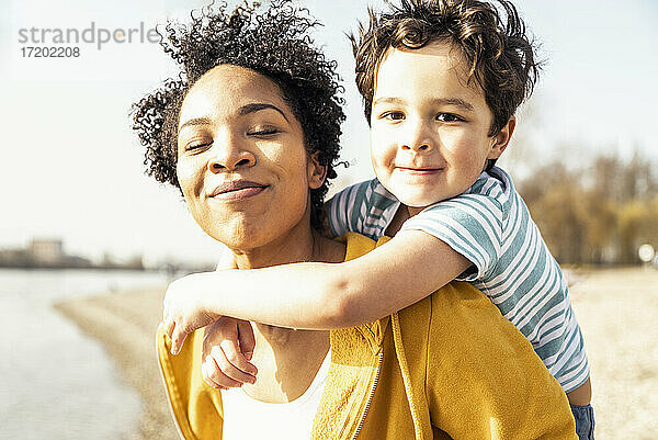 Lächelnde Mutter nimmt ihren Sohn an einem sonnigen Tag Huckepack