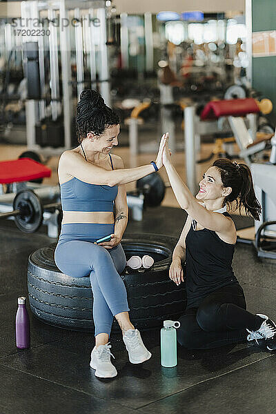 Glückliche Freundinnen geben sich High-Five  während sie im Fitnessstudio sitzen