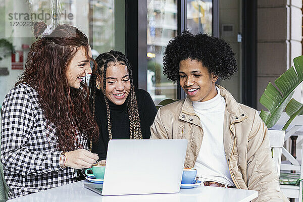 Studenten benutzen einen Laptop  während sie in einem Straßencafé zusammensitzen