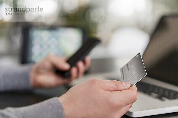 Hände eines Geschäftsmannes beim Online-Bezahlen mit Kreditkarte auf einem Mobiltelefon im Büro