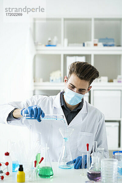 Ein männlicher Wissenschaftler füllt einen Kolben mit Medikamenten durch einen Trichter im Labor während COVID-19