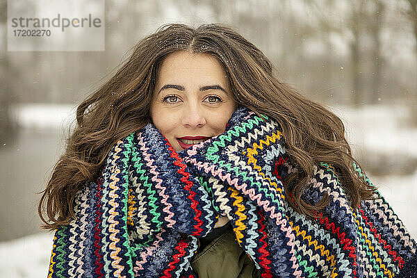 Lächelnde schöne Frau eingewickelt in bunte Decke im Winter