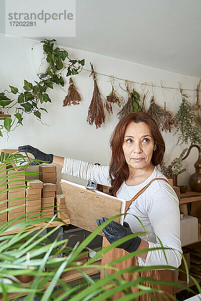 Besitzerin mit Klemmbrett  die Produkte in der Hand hält  während sie in der Werkstatt steht