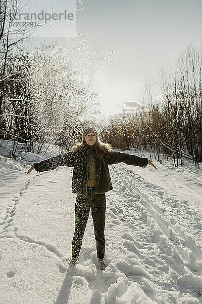 Porträt eines im Schnee stehenden Teenagers mit erhobenen Armen und geschlossenen Augen