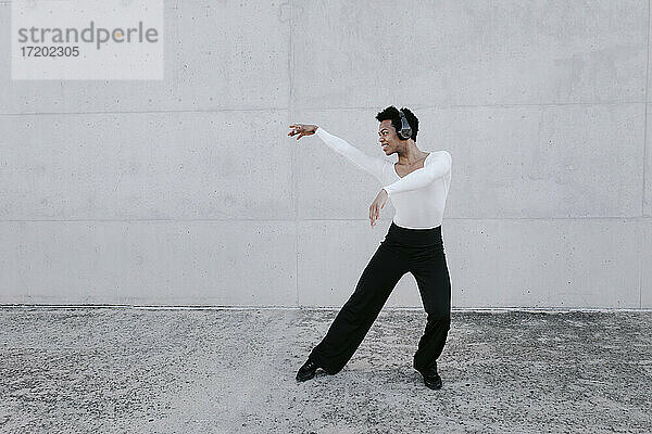 Flexibler Mann mit Kopfhörern  der gegen eine weiße Wand tanzt