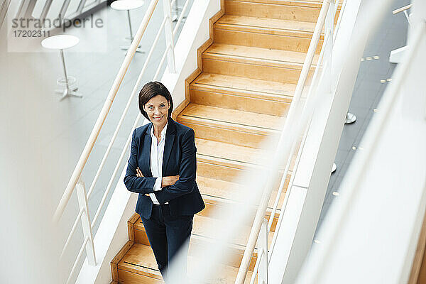 Selbstbewusste Geschäftsfrau mit verschränkten Armen auf einer Treppe im Korridor stehend