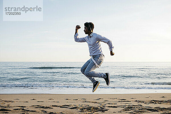 Mittlerer erwachsener Mann  der an einem sonnigen Tag am Strand springt
