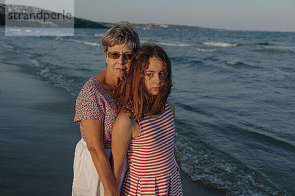 Enkelin steht mit Großmutter am Wasser am Strand