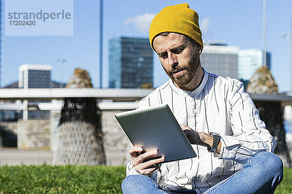 Gut aussehender Mann  der ein digitales Tablet benutzt  während er an einem sonnigen Tag im Park sitzt