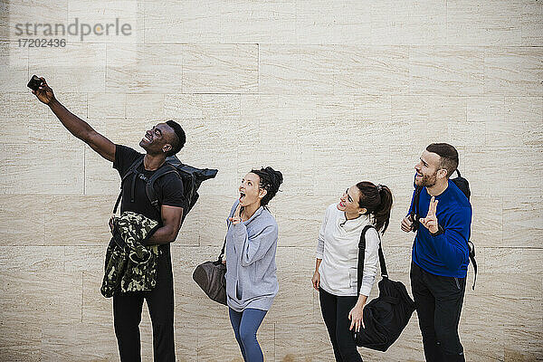 Fröhliche Athletenfreunde machen ein Selfie mit ihrem Smartphone an der Wand
